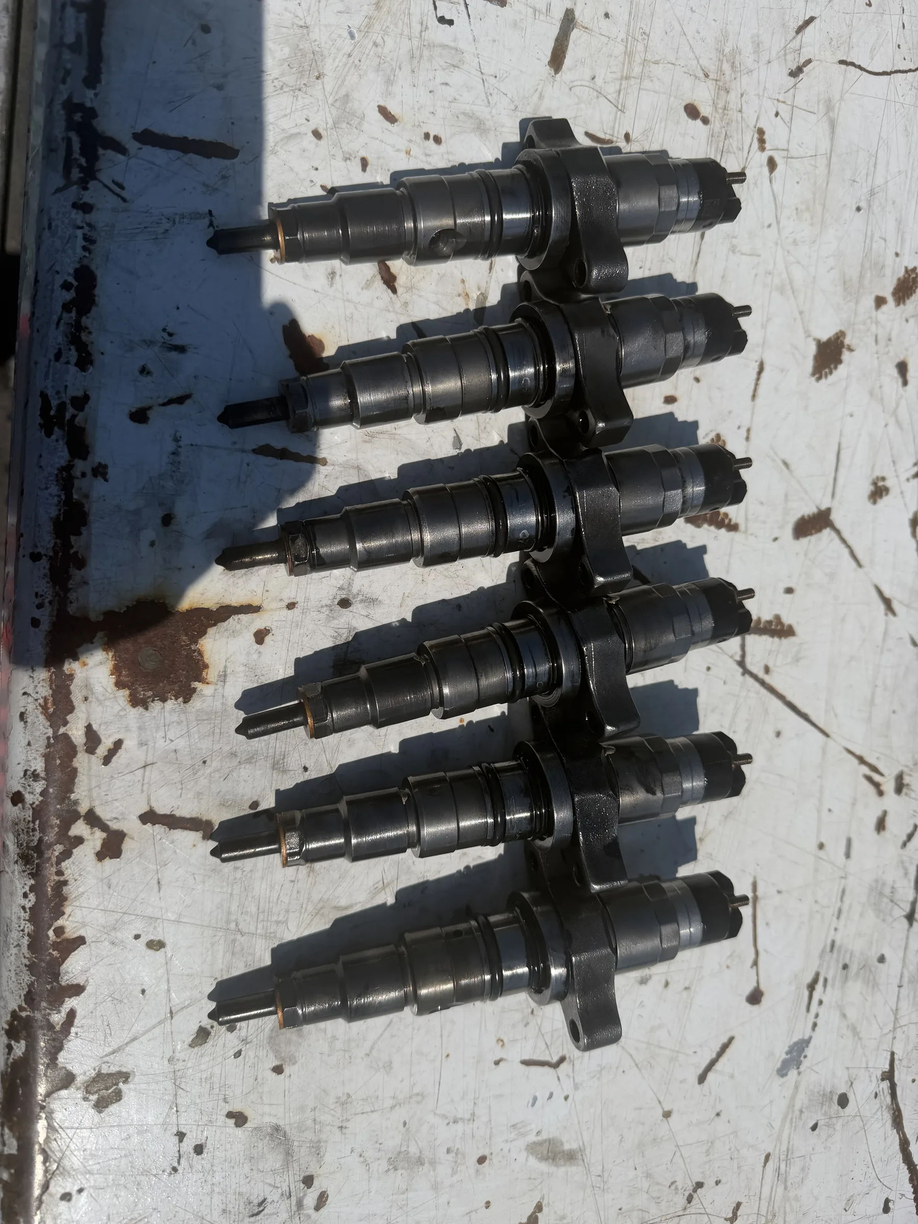 Six diesel fuel injectors lined up on a workbench